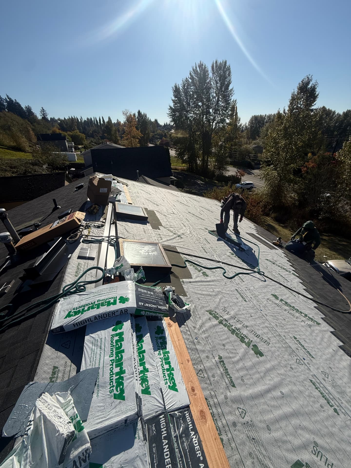 Roofers working on a roof covered in Malarkey synthetic underlayment, with shingle bundles lined up on the ridge