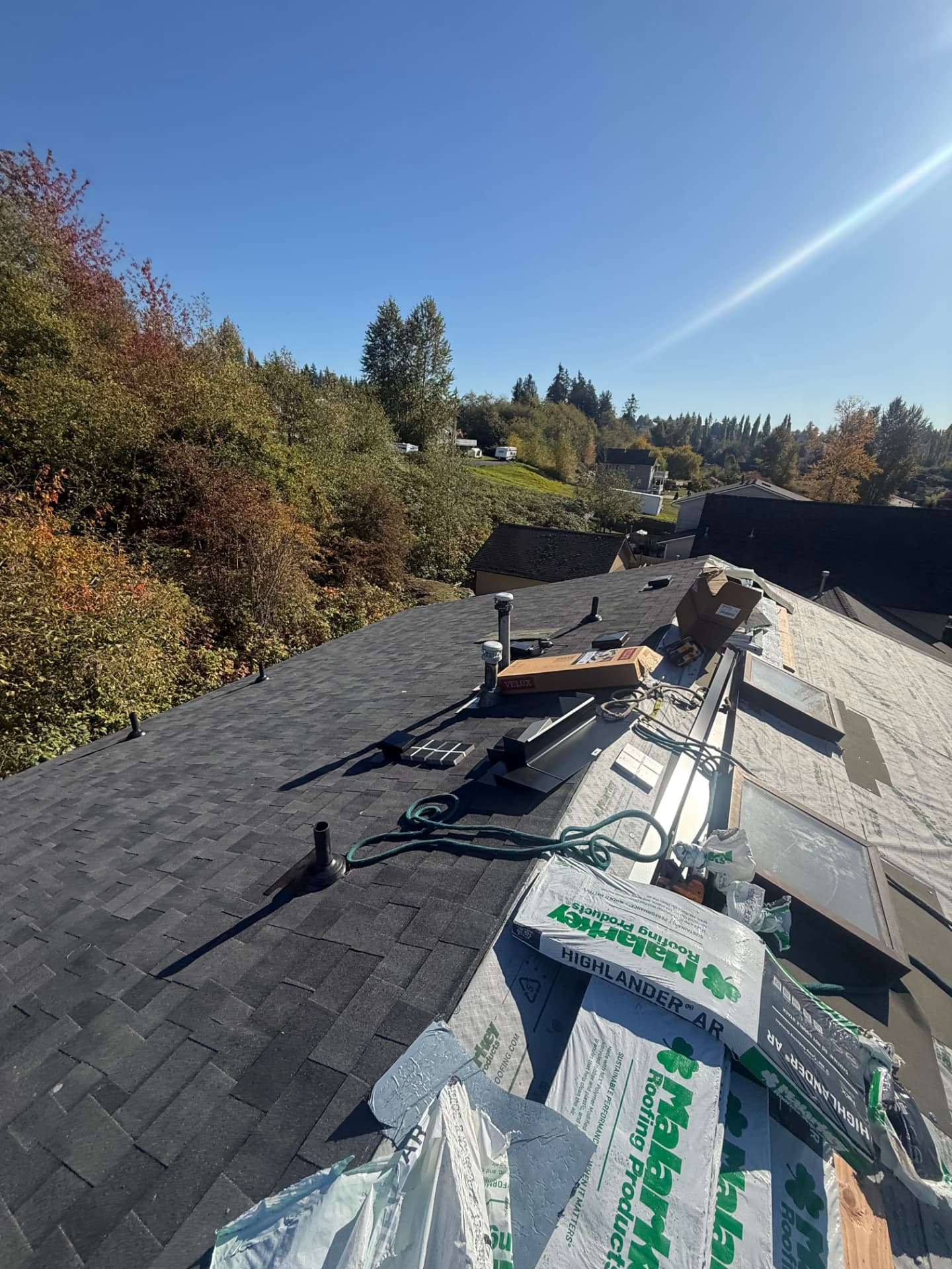 Bundles of Malarkey shingles and roofing tools staged along a roof ridge with new dark shingles on one side