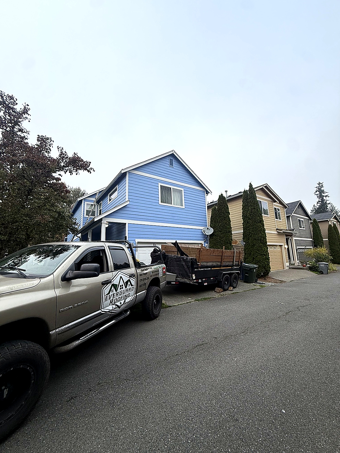 Everguard Roofing branded pickup truck with dump trailer parked outside a two-story blue house
