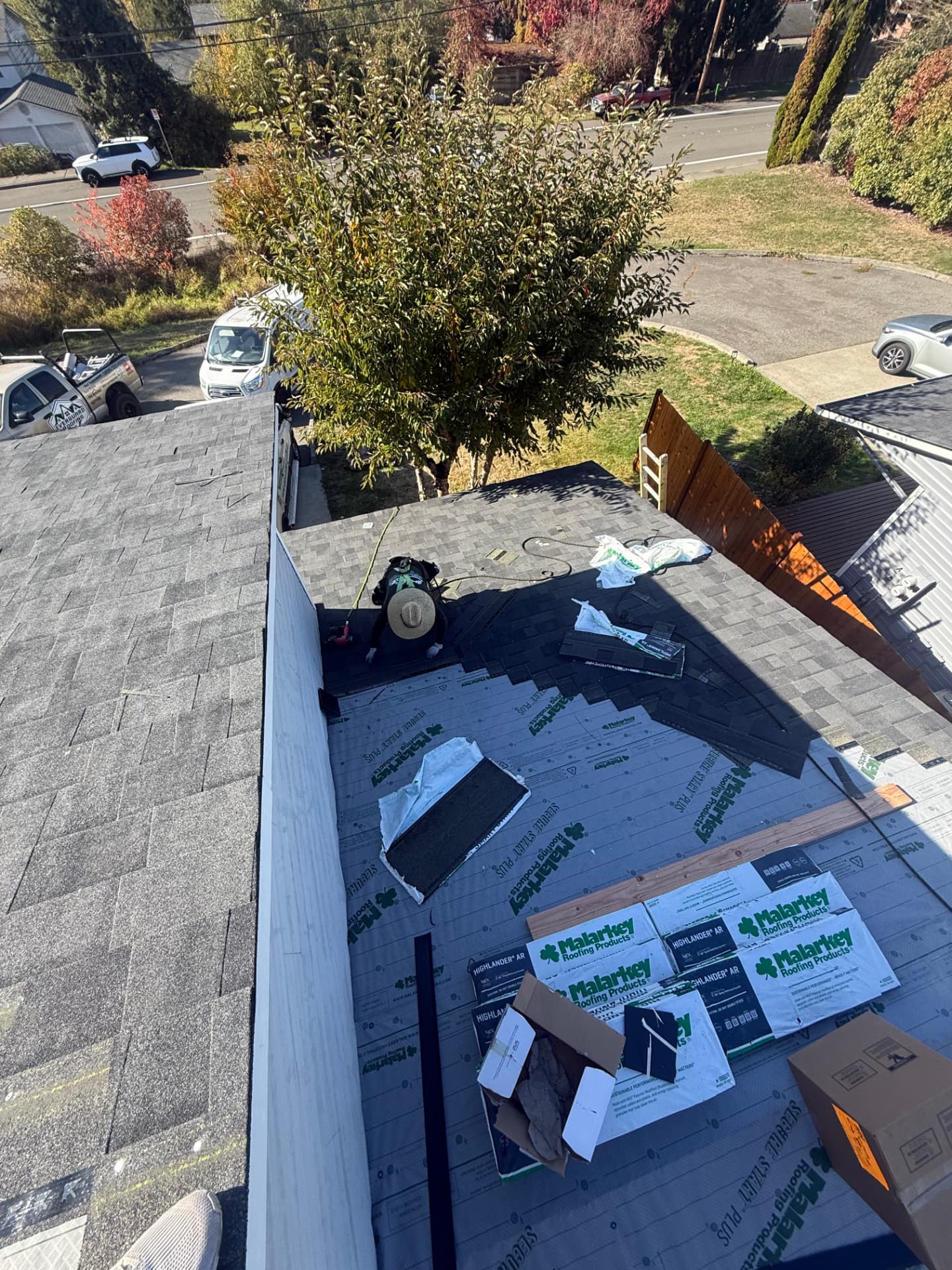 Overhead view of a roofer laying shingles across Malarkey synthetic underlayment with shingle bundles on the roof